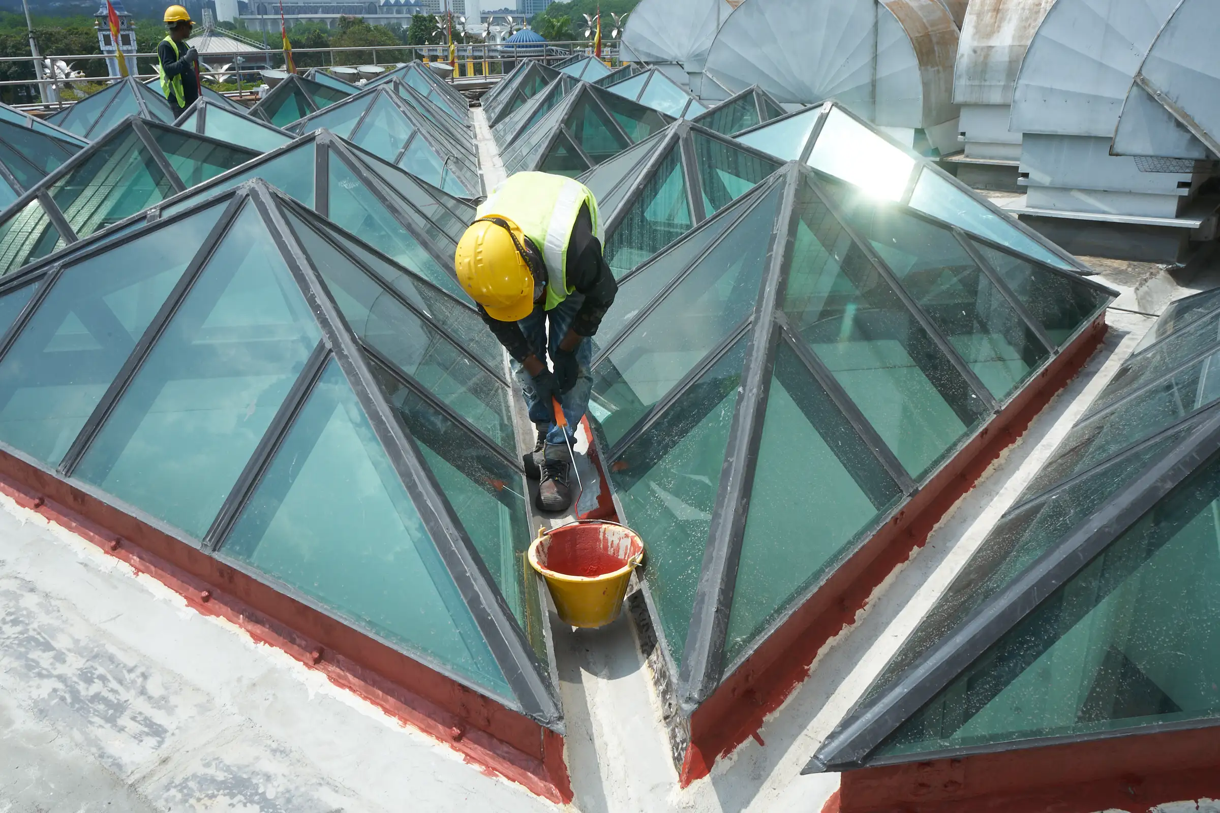 Worker sealing and waterproofing geometric rooftop skylights